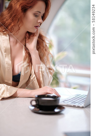 Woman in a bathrobe works on a laptop at home Woman in a bathrobe works on a laptop at home 58149234