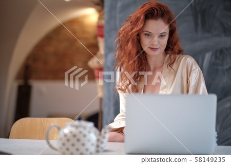 Woman in a bathrobe works on a laptop at home 58149235