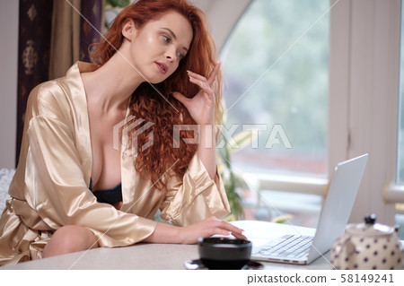 Woman in a bathrobe works on a laptop at home Woman in a bathrobe works on a laptop at home 58149241