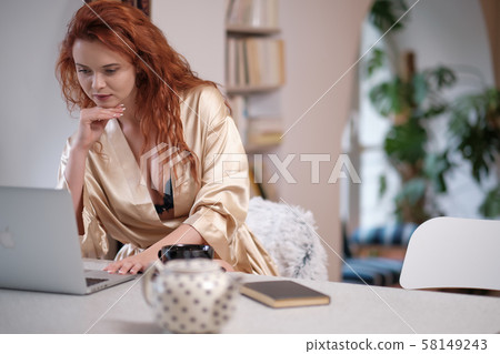 Woman in a bathrobe works on a laptop at home Woman in a bathrobe works on a laptop at home 58149243