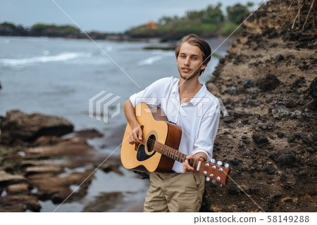 Romantic young man with a guitar on the beach 58149288