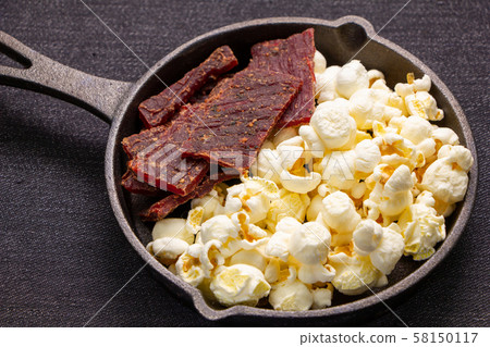 Popcorn and beef jerky. Assorted snacks on skillet. Popcorn and beef jerky. Assorted snacks on skillet. 58150117