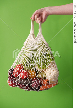 Female hand holding string eco bag with vegetables 58151400
