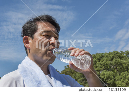 Middle-aged man drinking water after exercise in Yoyogi Park to combat heat stroke 58155109