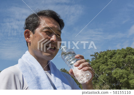 Middle-aged man drinking water after exercise in Yoyogi Park to combat heat stroke 58155110