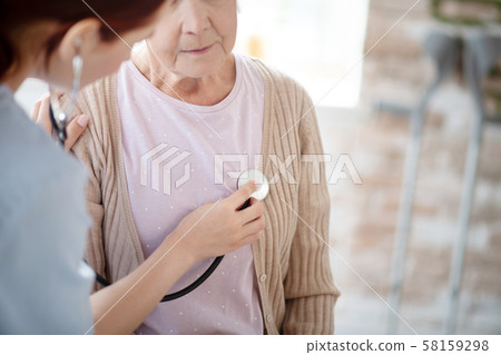 Caring nurse using stethoscope while examining retired woman Caring nurse using stethoscope while examining retired woman 58159298