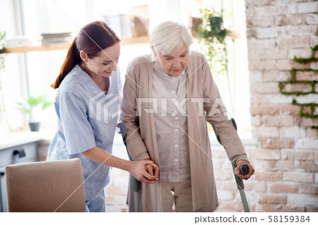 Helpful caregiver assisting woman with crutches Helpful caregiver assisting woman with crutches 58159384