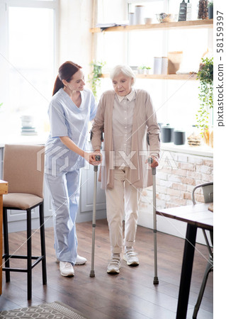 Caregiver assisting woman walking with crutches Caregiver assisting woman walking with crutches 58159397