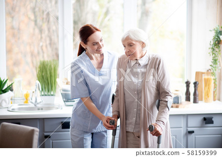 Smiling caregiver helping aged woman to make steps Smiling caregiver helping aged woman to make steps 58159399