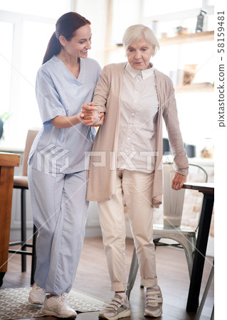 Aged woman making first steps after surgery on legs Aged woman making first steps after surgery on legs 58159481
