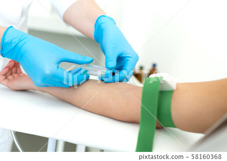 a gloved nurse inserts a needle into a vein on the a gloved nurse inserts a needle into a vein on the 58160368