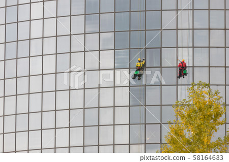 Two men workers cleaning the exterior windows of a skyscraper - industrial alpinism - hanging on Two men workers cleaning the exterior windows of a skyscraper - industrial alpinism - hanging on 58164683