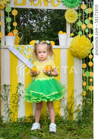 Little girl with orange near lemonade stand in 58171910