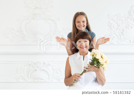 An elderly woman smiles and enjoys the mother's day surprise of her granddaughter. Selective focus An elderly woman smiles and enjoys the mother's day surprise of her granddaughter. Selective focus 58181382