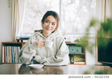 A woman who drinks coffee in a room A woman who drinks coffee in a room 58182356