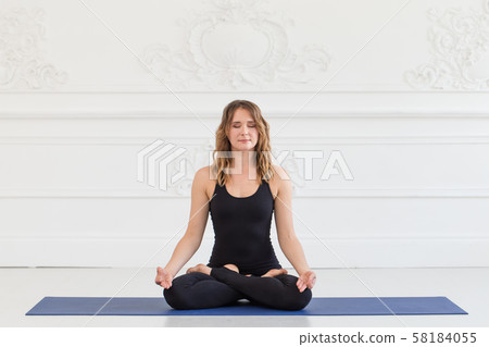 Beautifull woman in sport outfit stits in lotus pose on carpet 58184055