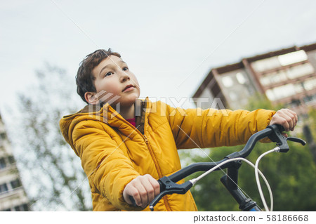 Cute tween boy in yellow jacket on bike in city Cute tween boy in yellow jacket on bike in city 58186668