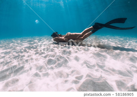 Freediver girl with fins glides over sandy sea in transparent ocean. 58186905