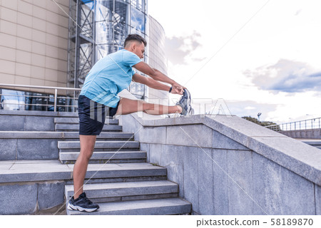 Male athlete, tanned man, summer in city, view from side, stretching muscles of legs knees ankle Male athlete, tanned man, summer in city, view from side, stretching muscles of legs knees ankle 58189870