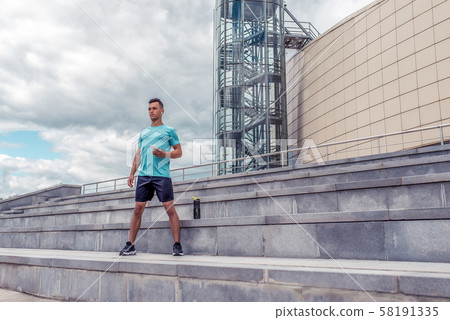 Male athlete in summer city listens to music with headphones, mobile phone, timer, time training 58191335