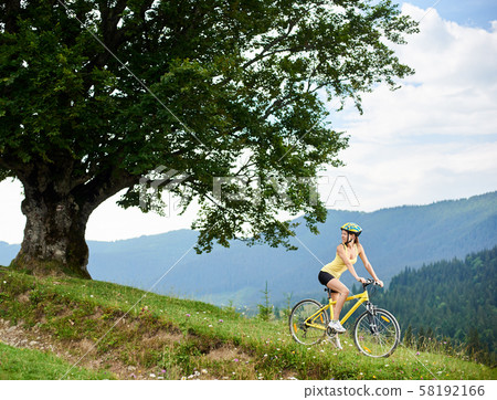 Attractive female cyclist with yellow mountain bicycle, enjoying sunny day in the mountains Attractive female cyclist with yellow mountain bicycle, enjoying sunny day in the mountains 58192166