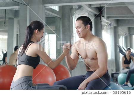 Healthy good looking Asian couple smiling and sitting together on gym ball at gym. Healthy good looking Asian couple smiling and sitting together on gym ball at gym. 58195616