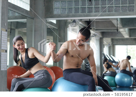 Healthy good looking Asian couple smiling and sitting together on gym ball at gym. 58195617