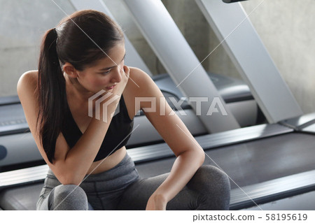 Good looking healthy Asian woman hurt after workout at gym. Gym equipment as background. 58195619