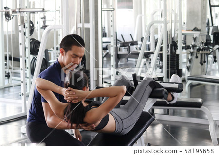 Asian healthy good looking man coaching and support healthy woman to use exercise equipment at gym Asian healthy good looking man coaching and support healthy woman to use exercise equipment at gym 58195658