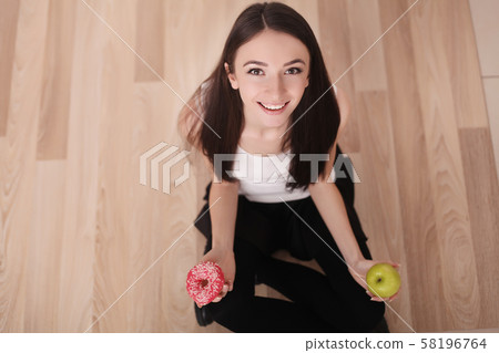 Diet. Woman Measuring Body Weight On Weighing Scale Holding Donut and apple. Sweets Are Unhealthy Diet. Woman Measuring Body Weight On Weighing Scale Holding Donut and apple. Sweets Are Unhealthy 58196764