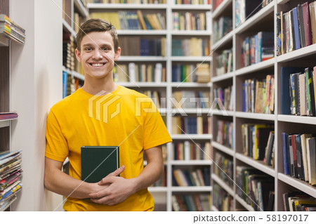 Cheerful male student standing between bookshelves in library Cheerful male student standing between bookshelves in library 58197017