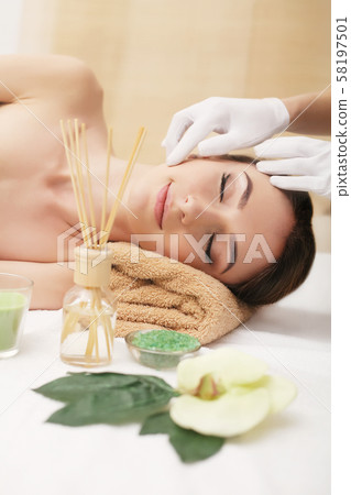 Beautiful young woman getting facial massage lying on the couch. Top view focused on the face Beautiful young woman getting facial massage lying on the couch. Top view focused on the face 58197501