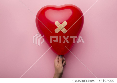 Woman holding Wounded heart with patch on pink background 58198000