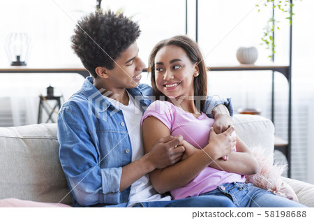 Tender teen couple sitting on sofa and cuddling each other Tender teen couple sitting on sofa and cuddling each other 58198688