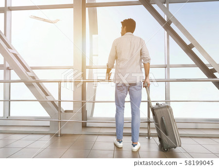 Young man with luggage enjoying window view at airport 58199045