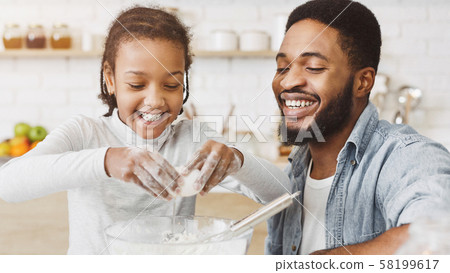 Cute black girl adding eggs into dough bowl 58199617