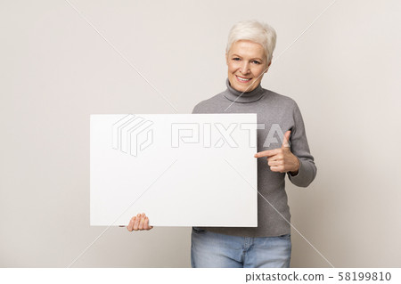 Senior woman holding blank advertising board and pointing on it 58199810