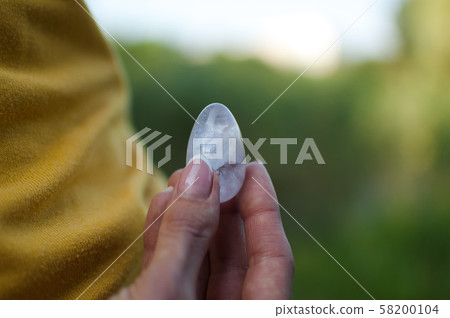 Adult girl in yellow shirt and blue jeans is holding transparent violet amethyst yoni egg for vumfit 58200104
