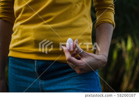 Adult girl in yellow shirt and blue jeans is holding pink quartz yoni egg for vumfit, imbuilding or 58200107