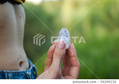 Side view of adult woman holding transparent violet amethyst yoni egg for vumfit, imbuilding or Side view of adult woman holding transparent violet amethyst yoni egg for vumfit, imbuilding or 58200110