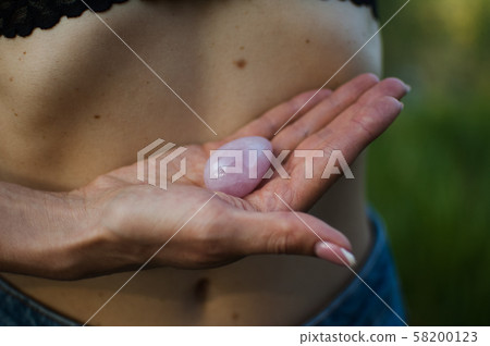 Adult woman is holding pink quartz yoni egg for vumfit, imbuilding or meditation outdoors over her 58200123