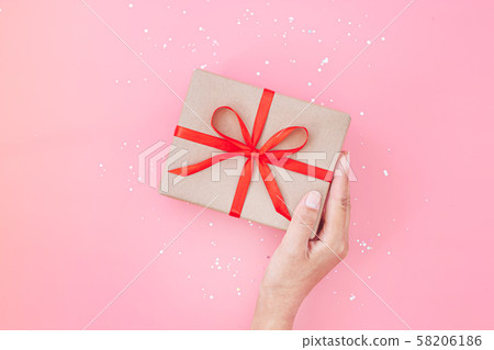 Female hands holding present box or gift box package in craft paper over pink background. Top view, flat lay 58206186