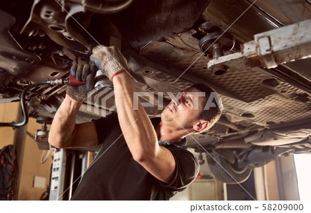 Repair man fixing car in repair station under lifted car during repair in garage 58209000