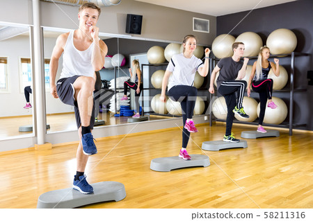 Smiling group raising legs on step platforms at fitness gym 58211316
