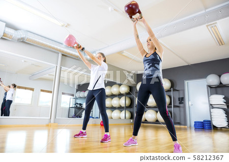 Two women trains with kettlebells at fitness gym 58212367