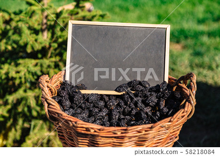 Basket full of oval shaped black prunes on field Basket full of oval shaped black prunes on field 58218084