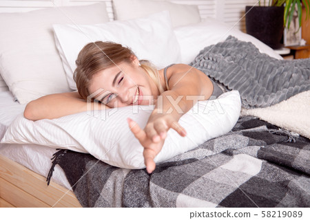 Young happy girl sitting on the bed in the morning, wrapped in a white blanket enjoying the morning. 58219089