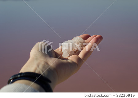 Female hand holding natural salt crystals on the background of a salt lake view from above 58220919