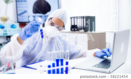 Caucasian scientist analyzes the tube and make some notes on laptop 58221454
