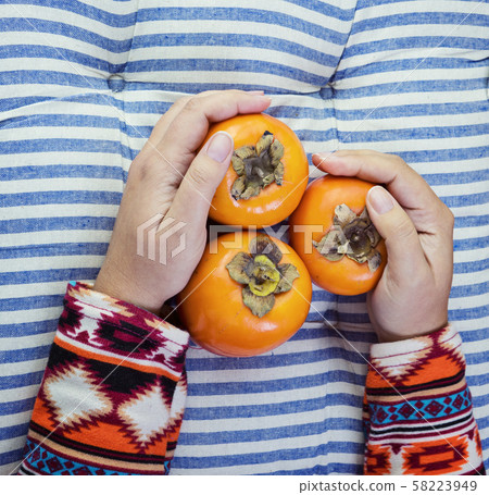 Female Hand holds three ripe persimmon on striped 58223949